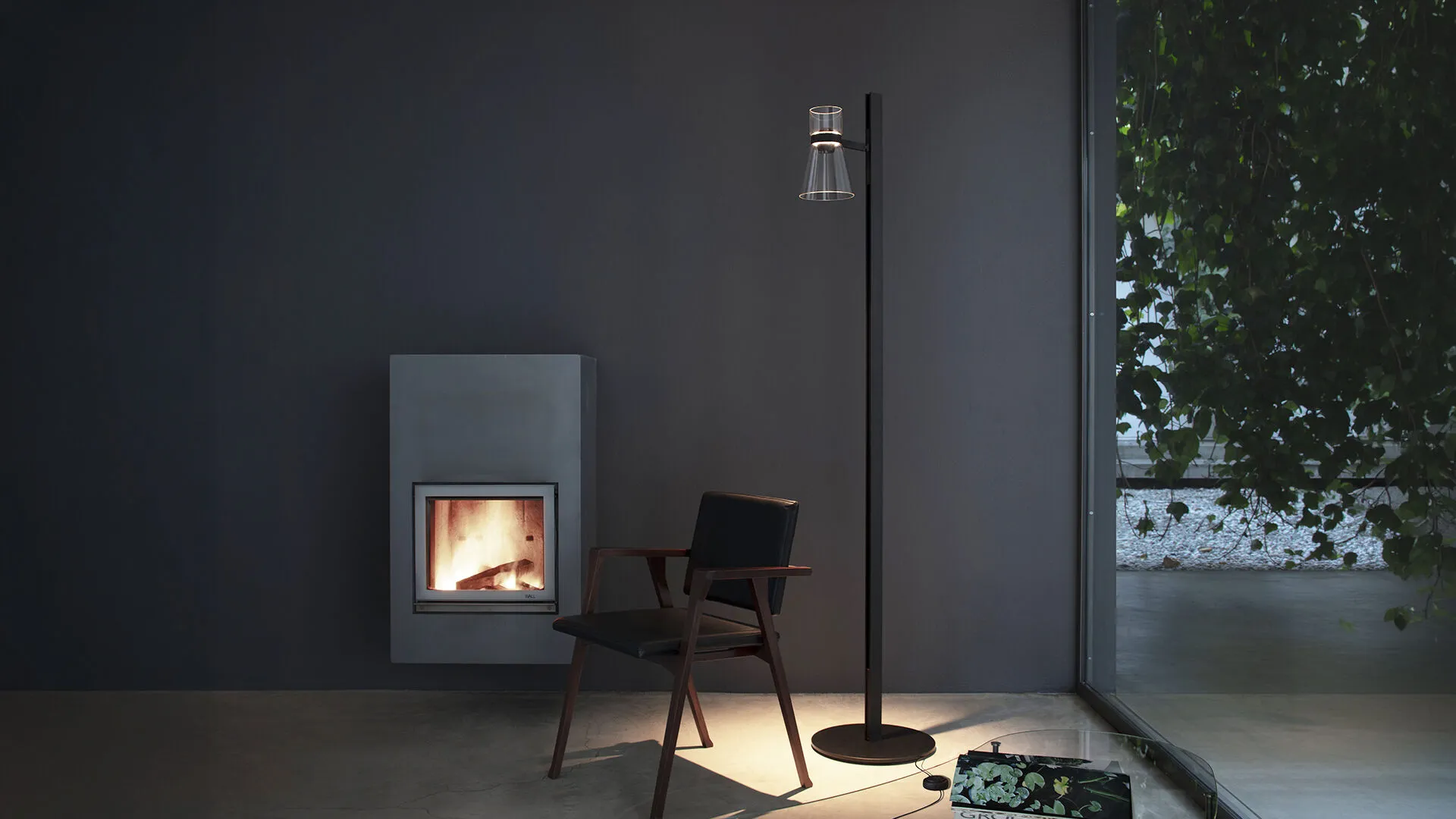 A residential interior at dusk lit by a single floor lamp and a fire